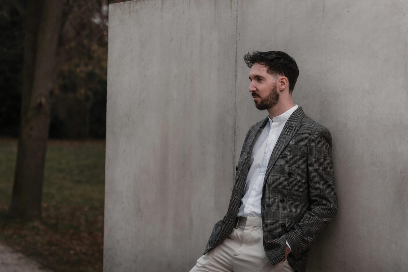 A fashionable man leaning against a wall in Graz, showcasing elegant menswear style.